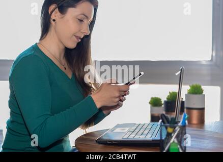 Woman using smart phone in front of laptop Stock Photo