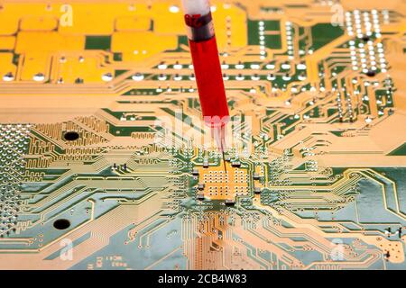 motherboard with contact paths of microcircuit and syringe with needle filled with red liquid, concept on topic of cospirology of vaccination and chip Stock Photo