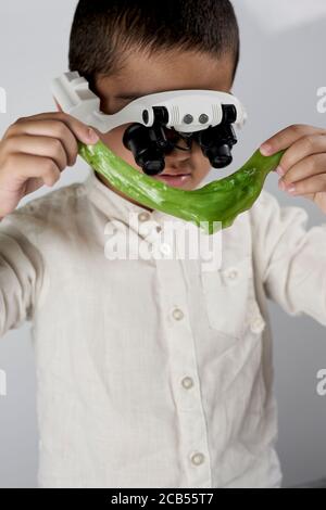 A small boy wearing special magnifying glasses and busy with interesting scientific experiments on slime at the workshop Stock Photo