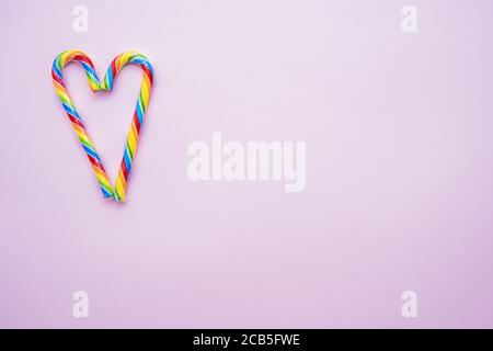 multicolored candy canes in the form of a heart on a pink background, copy space Stock Photo