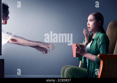 Asian woman scared with zombies coming out from the tv Stock Photo