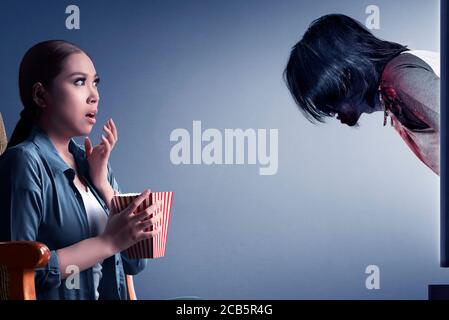 Asian woman scared with zombies coming out from the tv Stock Photo