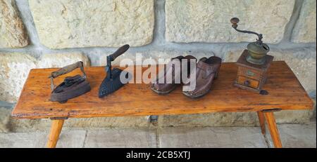 wo old rusty antique iron with wooden handle, hand coffee grinder and leather clogs on old wooden bench with sandstone wall background Stock Photo