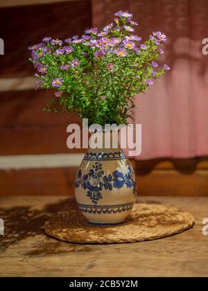 bunch of pink violet flowers in rustic ceramic painted vase on oak wood table in timbered cottage house Stock Photo