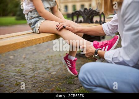 Little female child sitting on the wooden bench in the park Stock Photo