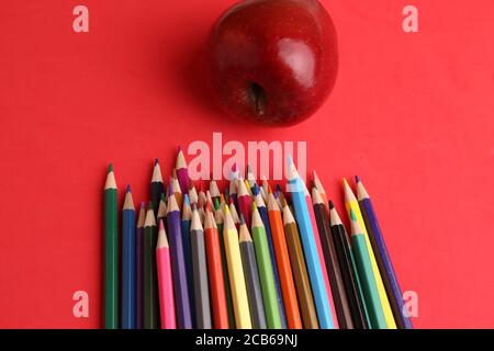 Red apple and colorful pencils on a red background Stock Photo