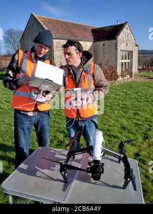 Two men prepare to fly a drone with a camera over a private garden and converted barn in the Cotswolds Stock Photo