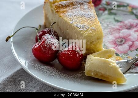 cheesecake and  cherries on a white plate and a napkin with flower pattern