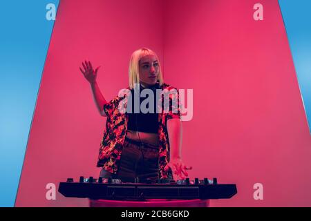 Mood. Young female stylish, fashionable musician performing on blue-red background in neon light. Concept of music, hobby, festival, entertainment, emotions. Joyful party host, DJ, portrait of artist. Stock Photo