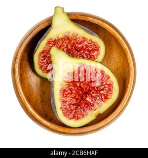 Fresh fig cut in two halves, in a wooden bowl. Fruit with purple skin and red flesh. Common figs can be eaten fresh, dried or as jam. Ficus carica. Stock Photo