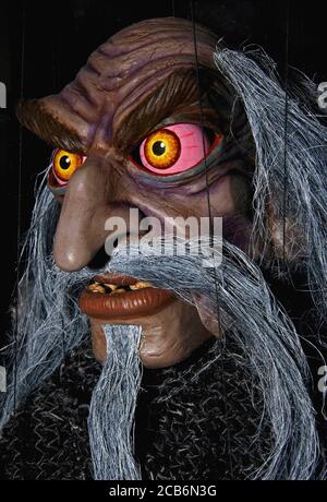 Wooden wizard puppet with pink and yellow bloodshot eyes, rotting teeth and facial hair made of wire.  In shop window of traditional mannequin retailer in Prague, Czechia / Czech Republic. Stock Photo