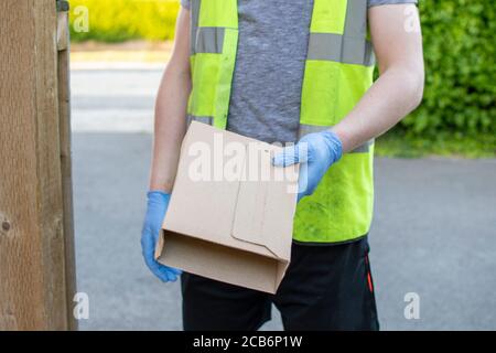 Delivery driver wearing rubber gloves handing over a parcel from a distance to avoid catching coronavirus or covid-19 during the pandemic where people Stock Photo