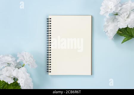 Spiral Notebook or Spring Notebook in Unlined Type and White Flowers at Top Right Corner and Bottom Left Corner on Blue Pastel Minimalist Background Stock Photo