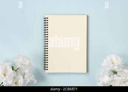 Spiral Notebook or Spring Notebook in Unlined Type and White Flowers at Bottom on Blue Pastel Minimalist Background Stock Photo
