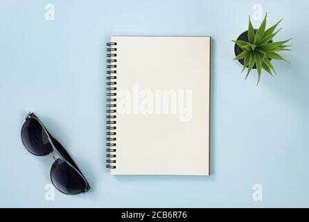 Spiral Notebook or Spring Notebook in Unlined Type and Office Plant and Sunglasses on Blue Pastel Minimalist Background Stock Photo