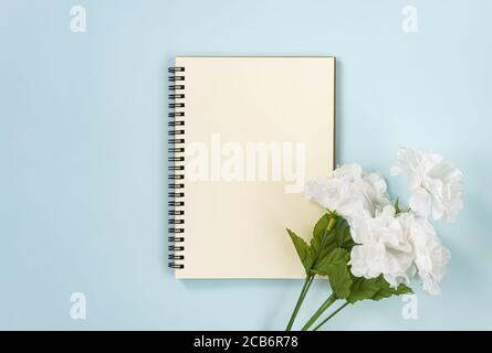 Spiral Notebook or Spring Notebook in Unlined Type and White Flowers at Bottom Right on Blue Pastel Minimalist Background Stock Photo