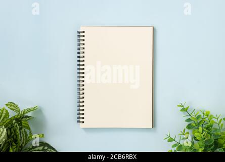 Spiral Notebook or Spring Notebook in Unlined Type and Office Plants at Bottom on Blue Pastel Minimalist Background Stock Photo