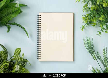 Spiral Notebook or Spring Notebook in Unlined Type and Office Plants at Corner on Blue Pastel Minimalist Background Stock Photo
