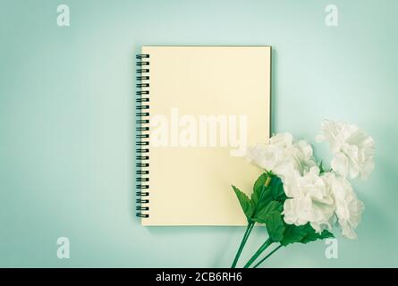 Spiral Notebook or Spring Notebook in Unlined Type and White Flowers at Bottom Right on Blue Pastel Minimalist Background in Vintage Tone Stock Photo