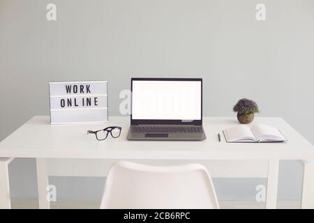 WORK ONLINE sign and laptop with blank screen on desk at home office, mockup for design. Stock Photo