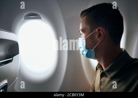Man wearing face mask inside airplane during flight. Themes new normal, coronavirus and personal protection. Stock Photo
