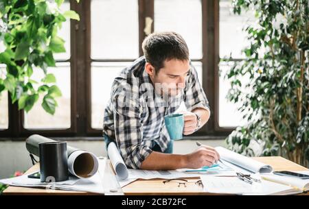 Architect working from home office studio on freelance renovation project. Young freelancer drawing his creative design idea for remote job. Hipster m Stock Photo