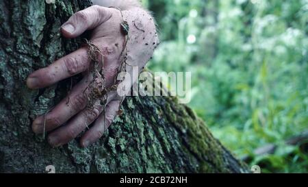 A horror concept of a mans hand holding on to a tree trunk covered in mud and plants Stock Photo