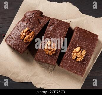 baked pieces of brownie chocolate cake with nuts on a brown piece of paper, top view, delicious dessert Stock Photo