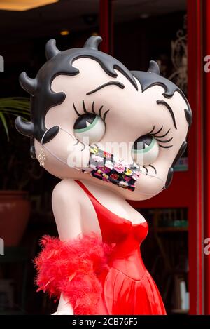 Betty Boop wearing a COVID-19 face mask. Large caricature of the Max Fleischer cartoon film star with a Coronavirus face covering. Red dress. Humorous Stock Photo