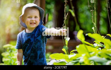 happy cheerful little boy having fun in garden. playing with plants. smiling and looking on camera Stock Photo