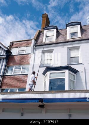 A windowcleaner cleaning windows with an extending pole and brush in Aldeburgh UK Stock Photo