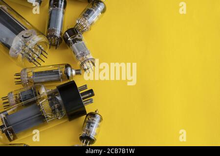 Random vacuum tubes on a yellow background. A group of radio tubes of different sizes and purposes. Copy space. Selective focus. Stock Photo