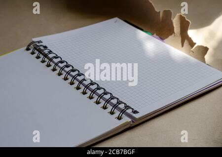 Open spring-bound notebook in sunlight. New diary with blank pages on torn wrapping paper. Side view at an angle. Selective focus. Stock Photo