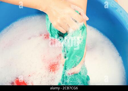 Closeup young Asian woman use hands washing color clothes in basin with detergent have soapy bubble water, studio shot background, laundry concept Stock Photo