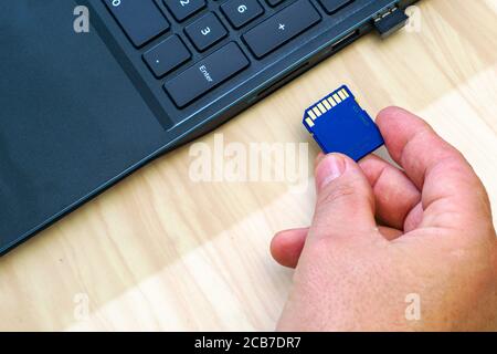 a man's hand inserting a flash card into a laptop connector Stock Photo