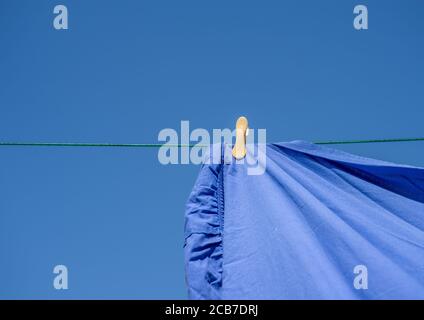 A yellow cloths peg on a washing line with a blue sheet and blue sky background. Stock Photo