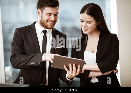 Successful business and modern technology concept. Young businesswoman and happy smiling businessman working together using tablet computer. Two Stock Photo