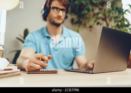 Young man in blue shirt sits at the table and studies with laptop Stock Photo