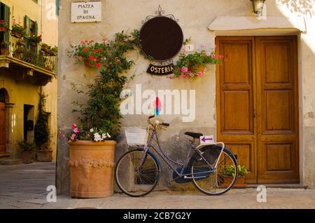 Facade of old osteria in Pienza with windows, flowers, wooden doors, plants and bycicle Stock Photo