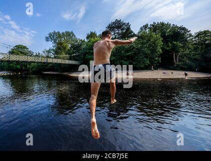 A person jumps from a rock into the River Wharfe near Ilkley in Yorkshire, as people continue to enjoy the hot weather. Stock Photo