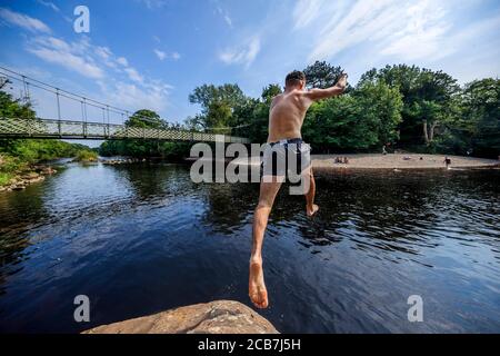 A person jumps from a rock into the River Wharfe near Ilkley in Yorkshire, as people continue to enjoy the hot weather. Stock Photo