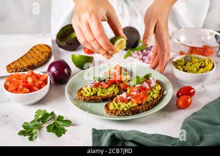 Close up of woman's hands squeezing a slice of lime on mashed avocado toast in a green plate Stock Photo