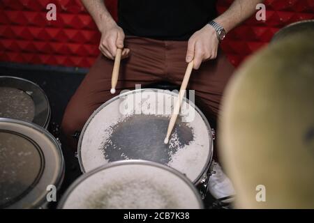Shot of an unrecognizable man playing the drums. Cropped view of man playing drums using wooden sticks in soundproof studio. Stock Photo