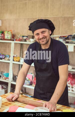 Male pastry chef using rolling pin on piece of dough. Making cake decoration Stock Photo