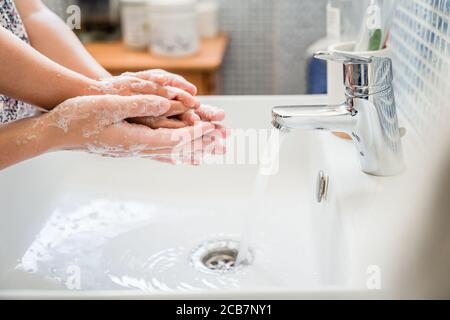 Mother and girl child washing hands together in bathroom sink with lots of soap under running water tap. side view Stock Photo