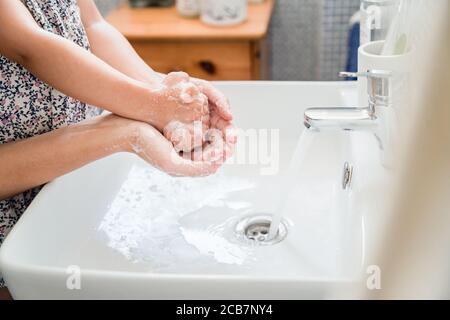 Mother and girl child washing hands together in bathroom sink with lots of soap under running water tap Stock Photo