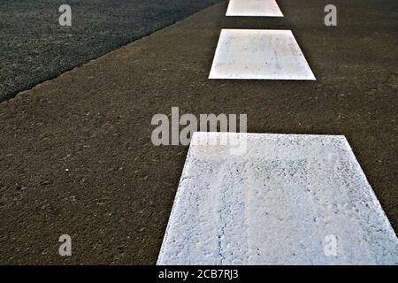 Broad dashed white line in perspective painted with reflective paint on black asphalt tarmac road. Stock Photo