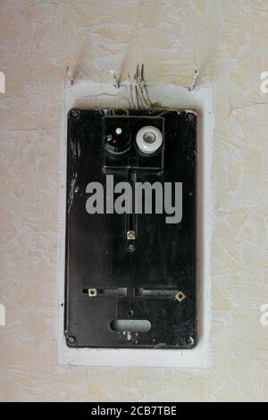 Very old black electrical fuses box hanging on white rural wall with copy space Stock Photo