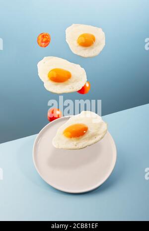 Three flying eggs and a plate on the modern blue background Stock Photo