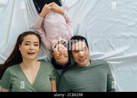 Asian mother and father lying with cute daughter on bed looking at camera and smiling. Happy family and togetherness lifestyle concept Stock Photo